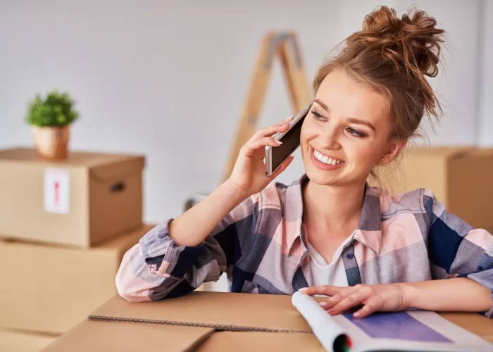 Eine Frau spricht auf ihrem Mobiltelefon, während sie zwischen Umzugskartons steht.